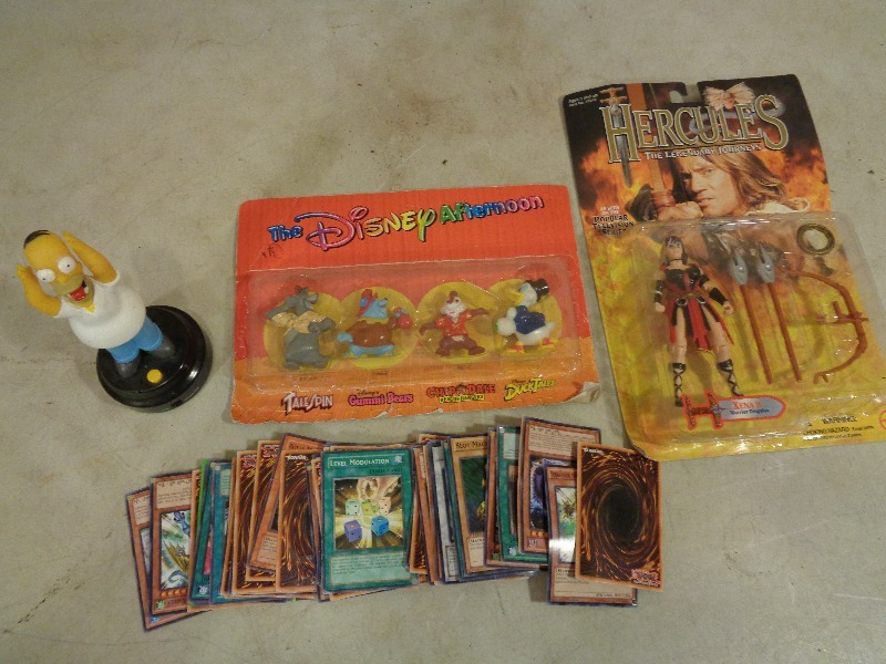 lot 39 image: New Hercules, Disney Afternoon Figures, Talking Homer SImpson, and Yu Gi Oh Cards