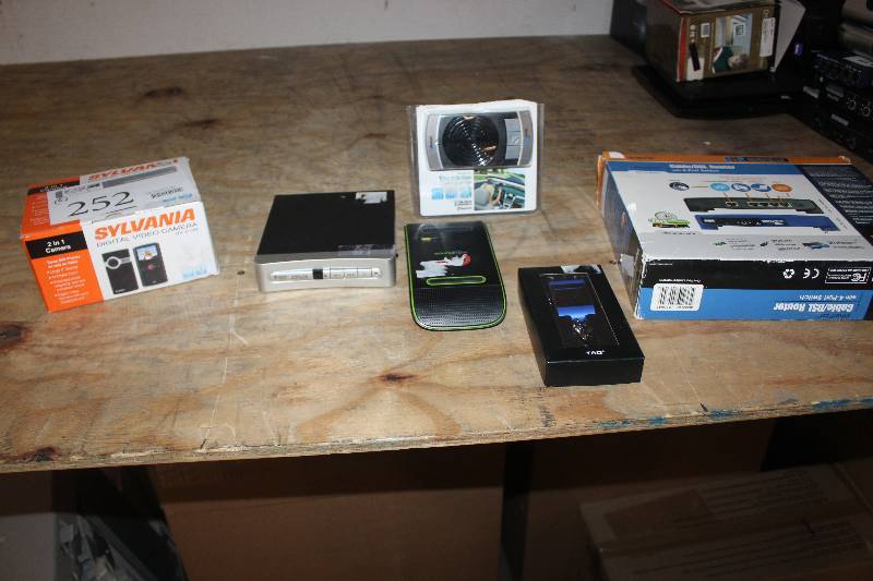 lot 252 image: Lot of (6) Electronic Equipment Including Sylvania Digital Video Camera Linksys DSLCable Router Analog Pass-Through Soundflow TAO Digital Photo Keychain True Blue