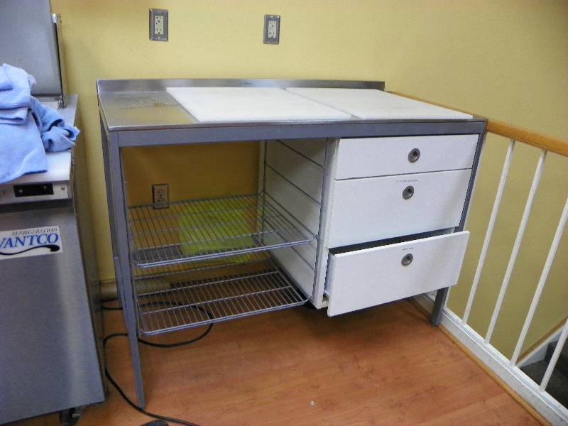 Prep station table with three drawers and two wire rack shelves.