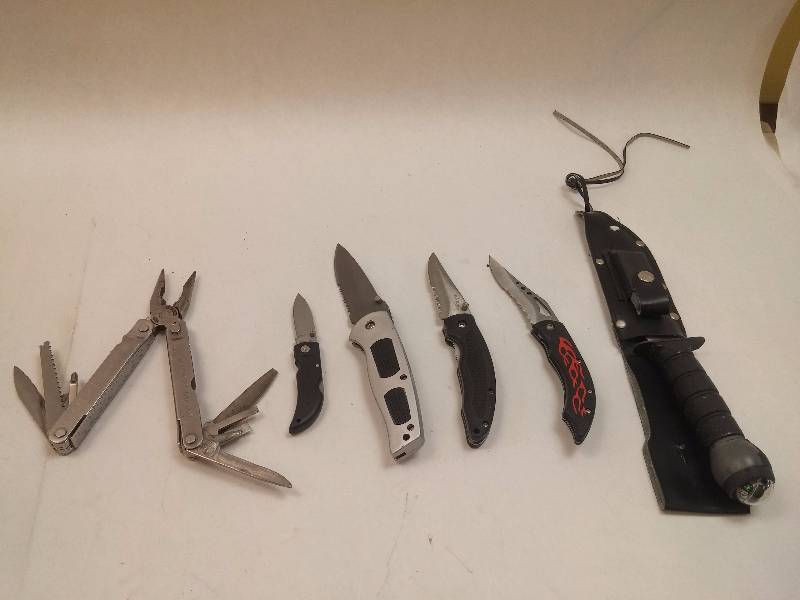 lot 838 image: Lot of 6 Various Knives Long Bowie  survival knife with sheath (missing strap), (2) Apache Black Stainless Flip Knife, Frost Barracuda Flip Knife, Silver Gray Frost Flip Knife, Leatherman Super Tool
