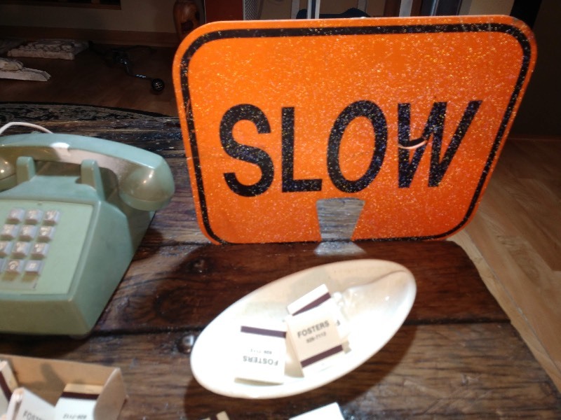 lot 74 image: Wood Wall Display Shelf w Cutouts of a Home and Trees, Yellow Face Mask of Helmet, Vintage Bell System Telephone Made by Western Electric, Orange Slow Traffic Sign, Box of Fosters Matches, White Ashtray