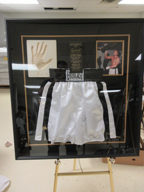 lot 702 image: MUHAMMAD ALI COLLAGE WITH SIGNED BOXING TRUNKS 2004