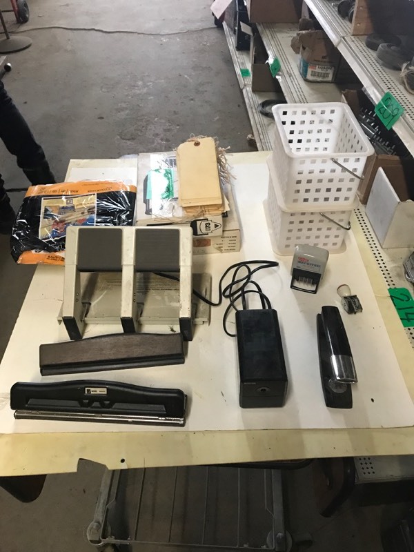 lot 249 image: Shelf of 2 staplers (1 electric), Two Plastic Baskets (new), One Ticket Dispenser Turn-o-Matic), One Now Serving Electronic Readout, Both new & Two paper punches & tags