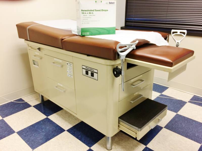 lot 42 image: MSRP $1200 Super Nice FAMILY PRACTICE OBGYN MEDICAL VETERINARIAN TREATMENT EXAMINATION TABLE WITH STEP UP STOOLS, TUCKAWAY STIRRUPS, STORAGE DRAWERS & 1 DOOR CABINET ALSO INCLUDES EXTRA PAPER ROLLS & FENESTRATED TOWELDRAPES