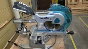 lot 1269 image: Makita LS1216L Double Bevel Sliding Compound Miter Saw with Laser, Attached Cabinet (60.5 x 28 x 37in.) Included. Powers on, appears to have a small broken plastic part, hence the Do not operate tag. Parts book included.