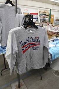 lot 449 image: Lot of (6) Long Sleeve T-Shirt Small White (x3), Grey (x3) with North Dakota Energizing America Logo (new)