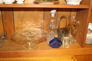 lot 776 image: Lot of (Approximately 7) Table Dcor (on shelf)  - Glass Cake Display, Large Glass Pitcher, Large Glass Vase, Glass Flower Basket, and more