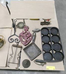 lot 15 image: Group of cast iron items.  Cast iron muffin pan, trivet, small square pan, 2 miniature sad irons, and a cast iron woodpecker toothpick retriever