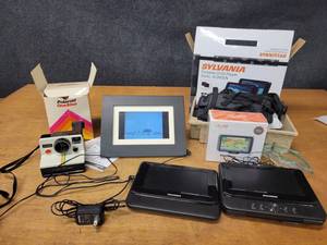 lot 276 image: Sylvania Portable Dual Screen DVD Player - Units Power On and Screens Work, Digital Picture Frame - Works, Polaroid One-Step Camera - Untested and NIB Mio Mov R403 GPS System