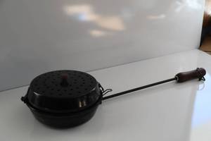 A Long Handled Pan With Attached Lid With Holes In It