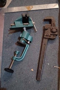 lot 506 image: Small Clamp-On Bench Vise - Like New, Aluminum Framing Square, Vintage Pipe Wrench and Three Meat Hooks