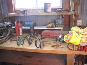 lot 347 image: All content on work bench including hay bale hooks, a hydraulic jack, a home made winch, safety vests, small round storage container filled with hardware, fire extinguisher, boxes of staples and so much more