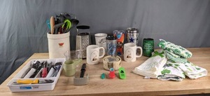 An Assortment of Kitchen Items Including Various Kitchen Utensils, Coasters, Mugs, Decorative Towels and More   C