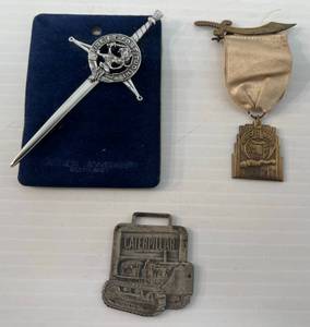lot 150 image: Group Of Vintage Items Including Sword Kilt Pin Carrick Clan Crest Badge, 1934 Minneapolis Shriners Medal And Vintage Caterpillar Crawler Tractor Watch Fob Schultz Machinery Co. Bismark - Minot Advertisment On Back