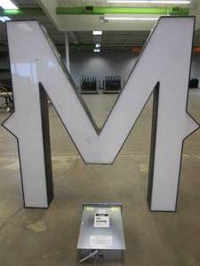 lot 104 image: Lighted Letter M Outdoor Signage With Transformer. Approximate Dimensions 44 x 5.25 x 42.5 Tall - USED FOR RETAIL BRAND MN HOME OUTLET.