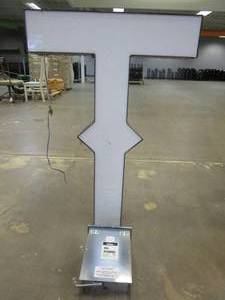 lot 108 image: Lighted Letter T Outdoor Signage With Transformer. Approximate Dimensions 29 x 5.25 x 42.5 Tall - USED FOR RETAIL BRAND MN HOME OUTLET.