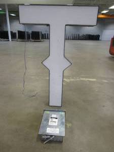 lot 111 image: Lighted Letter T Outdoor Signage With Transformer. Approximate Dimensions 29 x 5.25 x 42.5 Tall - USED FOR RETAIL BRAND MN HOME OUTLET.