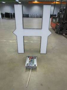 lot 115 image: Lighted Letter H Outdoor Signage With Transformer (Missing Plate Cover). Approximate Dimensions 35 x 5.25 x 42.5 Tall - USED FOR RETAIL BRAND MN HOME OUTLET.