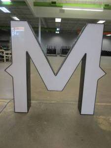 lot 124 image: Lighted Letter M Outdoor Signage, Transformer Not Included. Approximate Dimensions 30 x 5.25 x 28 Tall - USED FOR RETAIL BRAND MN HOME OUTLET.