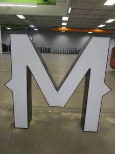 lot 128 image: Lighted Letter M Outdoor Signage, Transformer Not Included. Approximate Dimensions 30 x 5.25 x 28 Tall - USED FOR RETAIL BRAND MN HOME OUTLET.