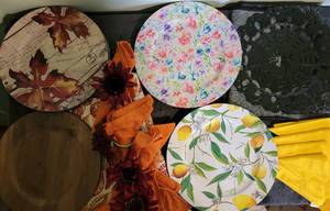 lot 83 image: Miscellaneous table decor- 4 lemon chargers with yellow cloth napkins, 2 halloween chargers with spider web runner, 4 flower chargers, 3 wood chargers, 3 fall leaf chargers, 4 orange cloth napkins with flower napkin holders, round table cloth fall leaves