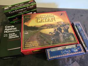 lot 110 image: Board games- Settlers of Catan (includes player expansion up to 6), Cards against humanity with small expansion, The oregon Trail card game, 2 boxes of poker chips