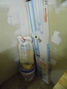 lot 39 image: Corner lot with bucket and partial bag of joint compound along with a box of 4ft shop light replacement bulbs
