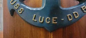 lot 113 image: Brass Colored Bell Mounted on a Blue Hook and Wooden Shelf, USS Luce - DD 522