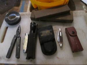 lot 477 image: Hardware bucket caddy with an assortment of pocket knives and multi-tool, whetstone and other supplies