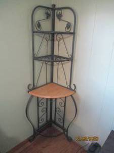 Green metal framed bakers rack style corner shelf with grapes and leaf designs and four tiers to display. One tier is wood while the others match the green metal petina frame.