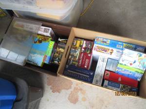 lot 52 image: (1) Fruit box and (1) Vintage flip top Storage Tote filled with a nice assortment of jigsaw puzzles in a variety of difficulty levels. (If any pieced were to be missing, it seems to be noted)