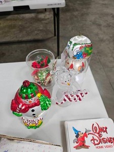 lot 71 image: A Walt Disney Christmas VHS, VTG Mickey & Minnie Skating Ornament, 1980s Smurf Silk Ball Ornament, Kitty Cucumber Musical Figurine, Mr. Christmas Snowman Hinged Wind Up Music Box w Rotating Skaters