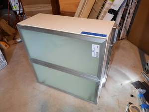 lot 298 image: IKEA AVSIKT Cabinet.  Door is white with frosted glass front 30.5 x 13 x 30 H. Portable cabinet light