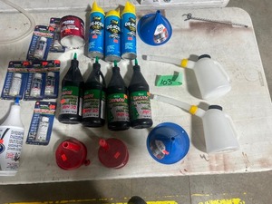 TABLE FULL OF HYDRAULIC OIL, FUEL TREATMENT, GREASE, DEICER,  & FUNNELS
