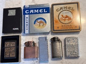 lot 204 image: Vintage Flip Top Lighter with Scene of Fairy & Mermaid in Camel Basma Tin, 1994 Zippo Camel Herd Black Crackle Brass Raised Emblem in Box, Vintage Camel Copper Tone Lighter, Camel Chrome Tone Lighter,  & Slim Lighter in Camel Lights Tin