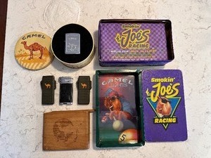 lot 215 image: Two 2003 Camel Butane Green Lighters and One Black and Chrome Lighter, Smoking Joes Racing Tin with Matches, Camel Lights Smoking Joe Ashtray, & Camel Wood Cigarette Holder, Vintage New Camel Collectors 1994 Zippo Lighter in Original Tin