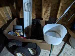 Box of misc camping supplies including a portable toilet, cut barrel for homemade shower, small tires, cookware pans and utensils plus more