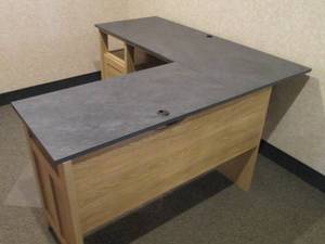 Light tone wood L-shaped desk with stone-look top, single door cubby and open shelf storage
