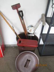 lot 112 image: Rubbermaid style lidded garbage can with assorted shovels and other outdoor supplies and accessories