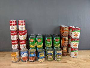lot 101 image: Assortment of Canned Goods - Bushs Baked Beans, Spaghetti-Os, Campbellss Soup, Del Monte Corn and Green Beans, and more H