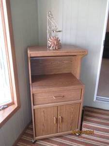 lot 63 image: Wood-tone Rolling Microwave cart with single drawer and 2-cupboard style doors plus brass tone shelf and Sun decor