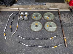 lot 216 image: Workout equipment 45 pound weight plates, 60 pound dumbbells, cable bars, and barbells