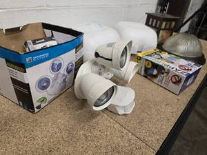 lot 55 image: Group of misc lights -  3-head motion activated light, exterior light, 2 white plastic replacement globe kits, flush mount interior light and 1 -  Zapplight