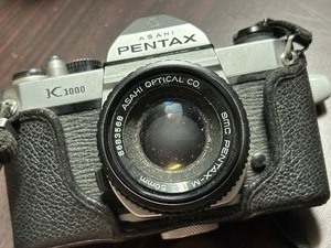 lot 112 image: Asahi Pentax K1000 Film Camera with partial case and strap with lens