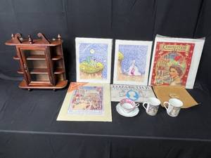 lot 73 image: Lot of Great BritainRoyal Family Themed Collectibles, Coronation Coloring Book, Tea Cup and Saucer Set, 2 Park Scene Heirloom China Mugs and Small Wooden Display Case w Glass Door