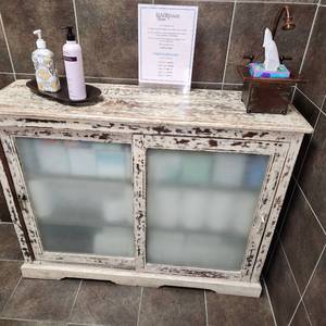 lot 63 image: Rustic Ivory Wood Cupboard Sideboard with Frosted Glass Sliding Doors and 3 Interior Shelves for Storage. Measuring 45-14 inches W by 13-12 inche D by 35 inches H. Cabinet only, contents not included