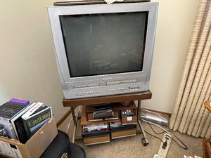 lot 96 image: Magnavox Console Television with Built in VHS and DVD Players. TV Stand and Cases of VHS Cassettes and VHS Rewinder.