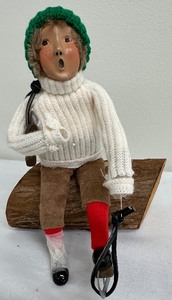 lot 192A image: Byers Choice Ltd - The Carolers - Child Skater Lacing Up Sitting on a Log with Green Stocking Cap - 1993
