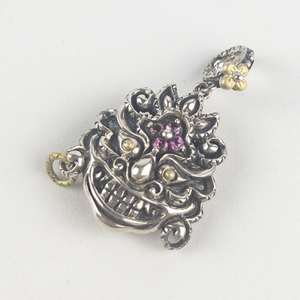 lot 63 image: Barbara Bixby Rhodolite Tibetan mask sterling and 18K yellow gold charm. Estimated Replacement value $155