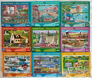 lot 42 image: Mega Puzzles Hometown Collection 1000pc Puzzles -Bundle of 9 Puzzles